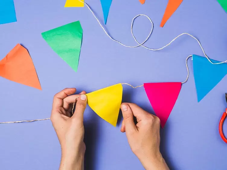 A pair of hands cutting paper bunting with scissors on a blue background. Created for Asian Paints.