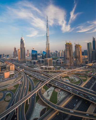 Aerial view of Dubai real estate skyline featuring the Burj Khalifa and complex highway interchanges during sunrise.