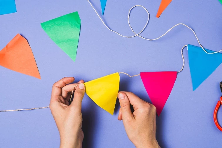 A pair of hands cutting paper bunting with scissors on a blue background. Created for Asian Paints.